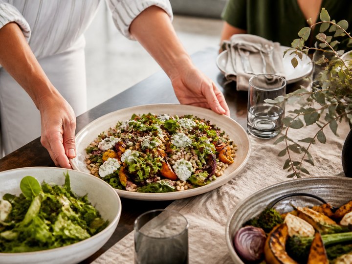 A healthy grain and roasted vegetable lunch being placed on a table