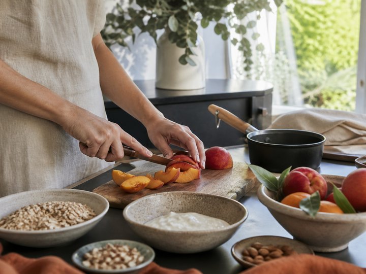 Stone fruit being sliced beside oats, nuts and yoghurt